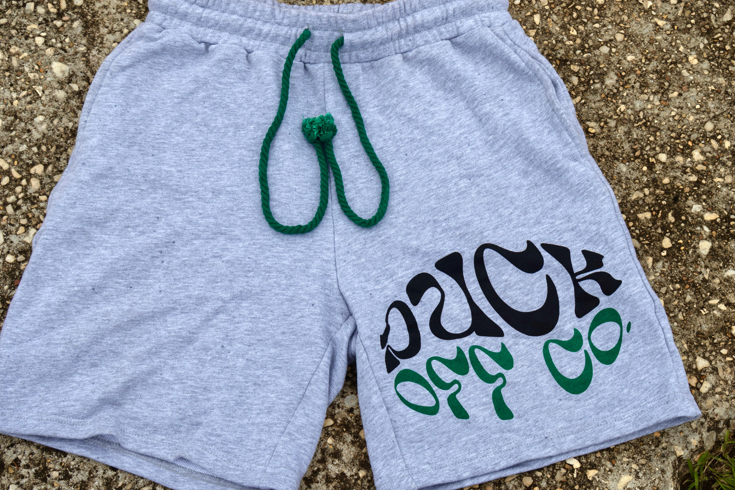Gray shorts with text and green drawstring on a textured surface