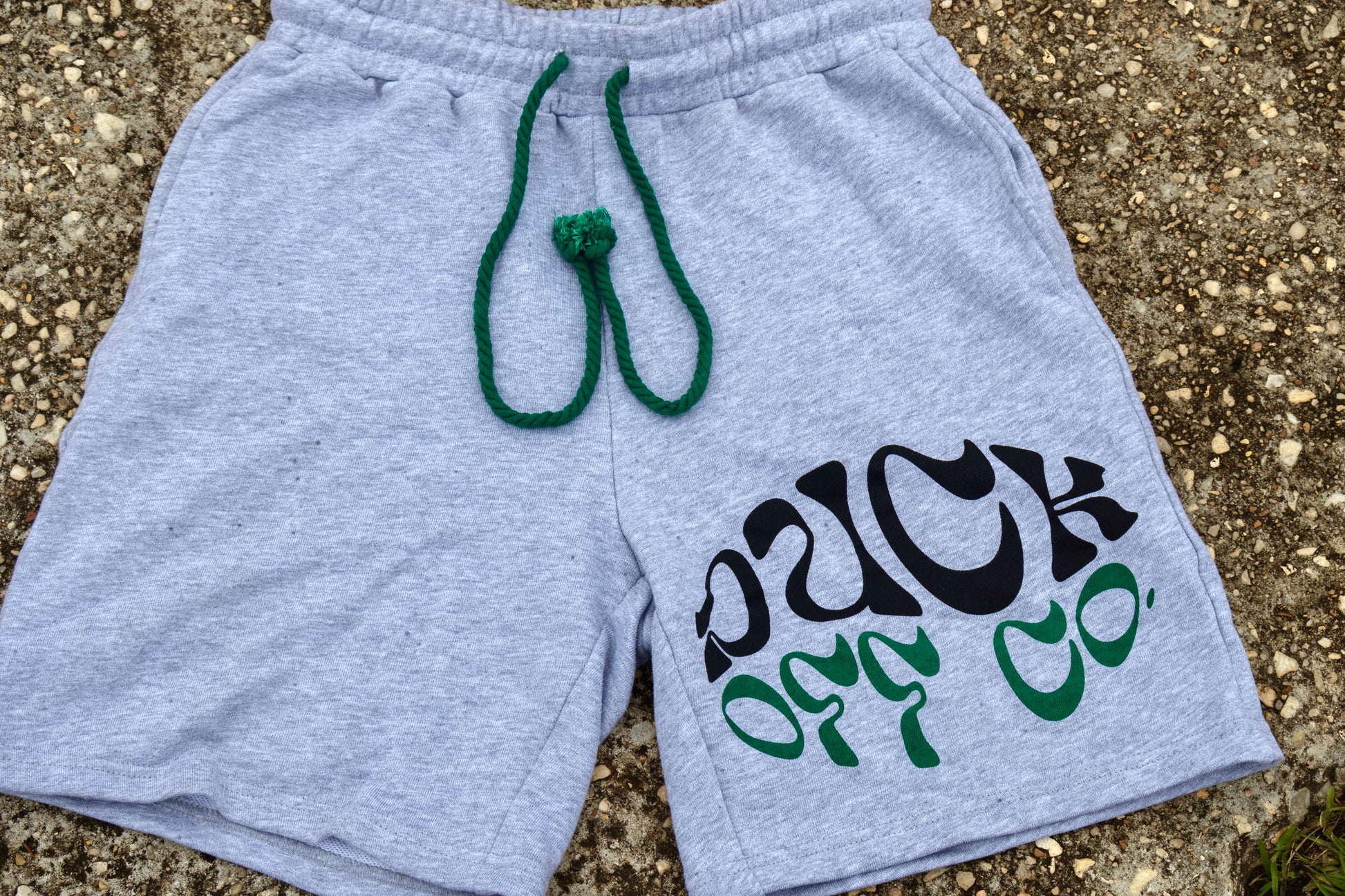 Gray shorts with text and green drawstring on a textured surface