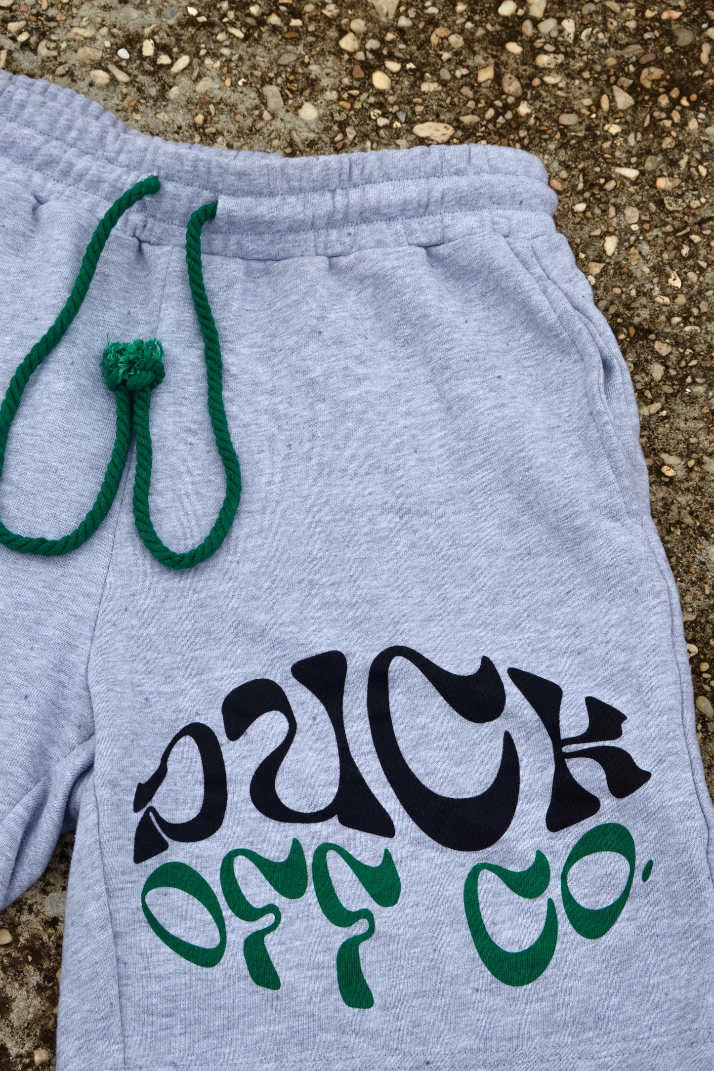 Gray shorts with black and green text on a concrete surface